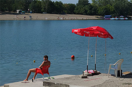 Deux parasols rouges, un gardien de plage et le lac de l’île d’Ada Ciganlija
